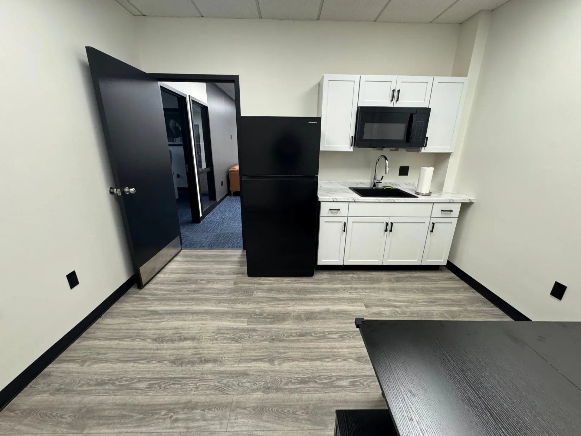 Client kitchenette at Shine Wellness & Recovery with white shaker cabinets, black appliances, and a marble-patterned countertop