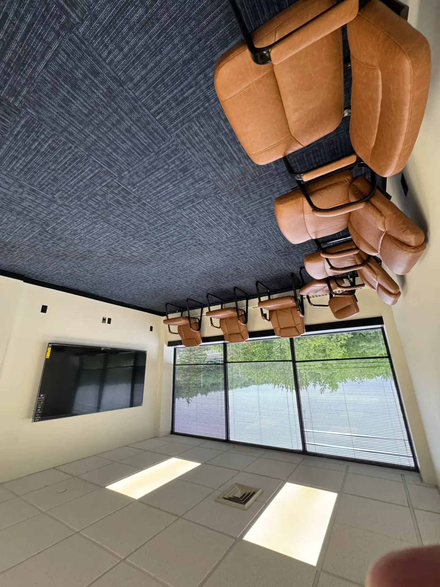 Small group room at Shine Wellness & Recovery with a row of brown leather chairs along a window wall, wall-mounted TV, and patterned carpet
